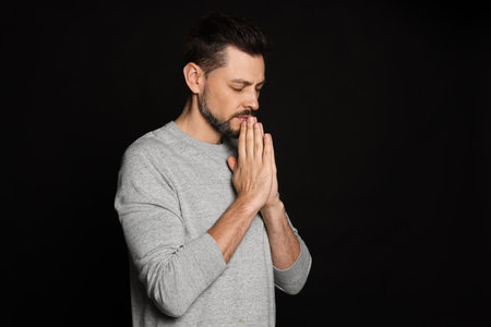 Man with clasped hands praying on black backgroundの写真素材