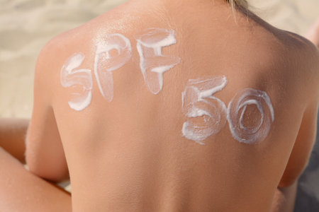 Child with abbreviation SPF 50 of sunscreen on back at beach, closeupの写真素材