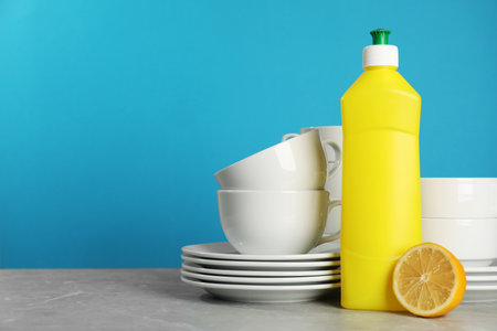 Clean tableware, dish detergent and lemon on gray table against light blue background. Space for textの写真素材