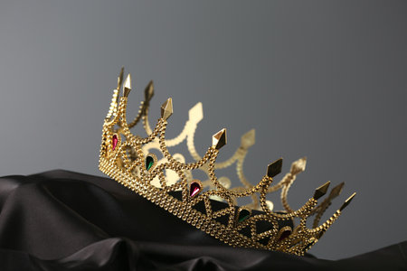 Beautiful golden crown with gems on dark cloth against gray backgroundの写真素材