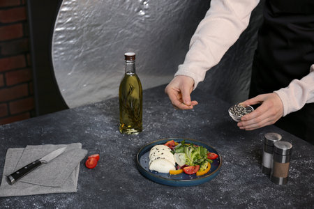 Food stylist preparing delicious salad with mozzarella and tomatoes for photoshoot at dark gray table in studio, closeupの写真素材
