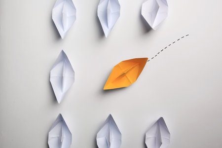 Yellow paper boat floating to others on white background, flat lay. uniqueness conceptの写真素材