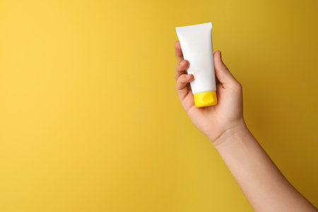 Woman holding tube of face cream on yellow background, closeup. Space for textの写真素材