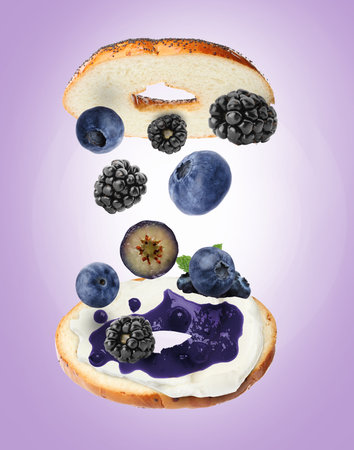 Tasty cut bagel with different ingredients flying on violet backgroundの写真素材