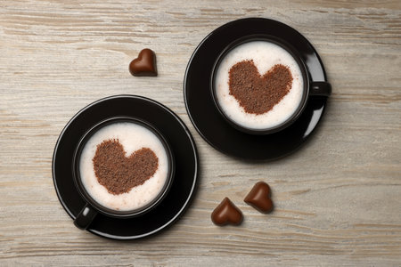 Cups of aromatic coffee with heart shaped decoration and chocolate candies on wooden table, flat layの写真素材