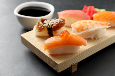 Wooden board with delicious nigiri sushi and soy sauce on black table, closeupの写真素材