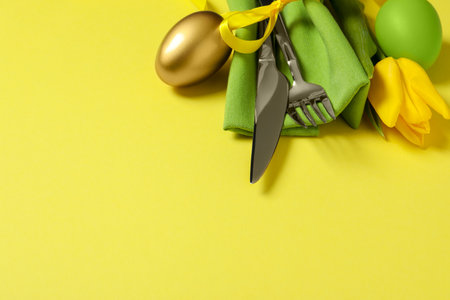 Cutlery set, painted eggs and beautiful flower on yellow background, space for text. easter...