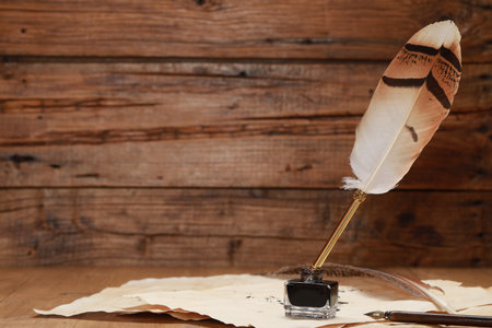 Inkwell with feather pen and vintage parchment on wooden table. Space for textの写真素材