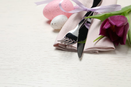 Cutlery set, painted eggs and beautiful flower on white wooden table, space for text. easter...