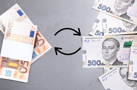 currency exchange. Circle arrows between hryvnias and euro banknotes on gray background, flat lay