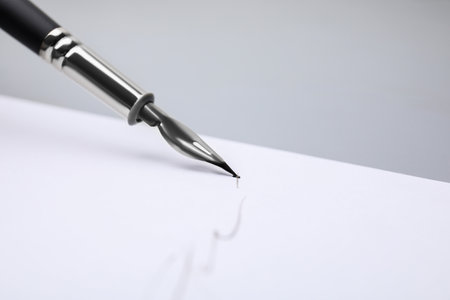 Signing on sheet of paper with fountain pen against light gray background, closeup. Space for text