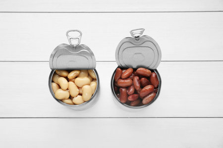 Tin cans with different canned kidney beans on white wooden table, flat lay