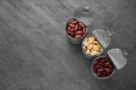 Tin cans with different canned kidney beans on gray table, flat lay. Space for text