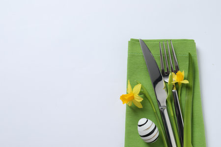 Cutlery set, Easter egg and narcissuses on white background, top view with space for text. Festive table settingの写真素材