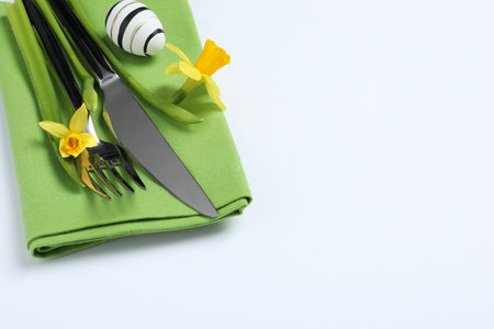 Cutlery set, Easter egg and narcissuses on white background, space for text. Festive table settingの写真素材