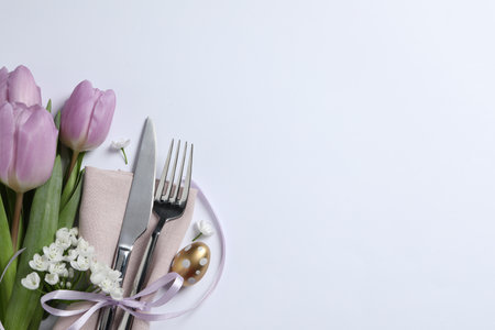 Cutlery set, Easter egg and beautiful flowers on white background, flat lay with space for text....