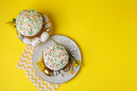 Traditional Easter cakes with sprinkles, painted eggs and beautiful spring flowers on yellow...