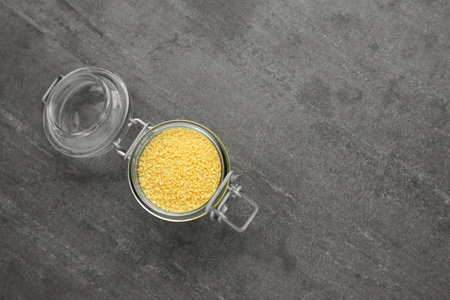 Glass jar of raw couscous on gray table, top view. Space for text