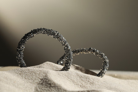 luxury jewelry. Stylish presentation of earrings in sand against gray background, closeup