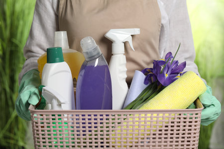 Woman holding basket with spring flowers and cleaning supplies outdoors, closeupの写真素材
