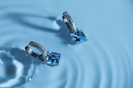 luxury jewelry. Elegant earrings in water on light blue background, space for textの写真素材