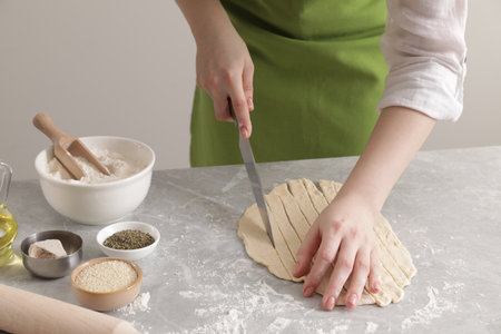Woman cutting dough at light gray marble table, closeup. Cooking grissini
