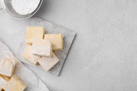 Delicious sweet marshmallows with powdered sugar on light gray table, flat lay. Space for text