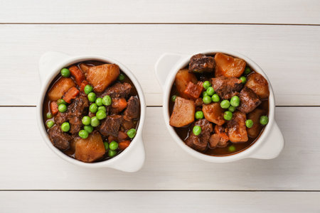 Delicious beef stew with carrots, peas and potatoes on white wooden table, flat layの写真素材