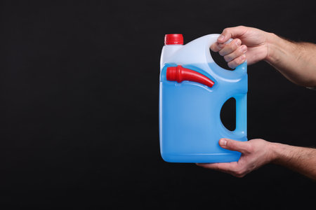 Man holding canister with blue liquid on black background, closeup. Space for textの写真素材