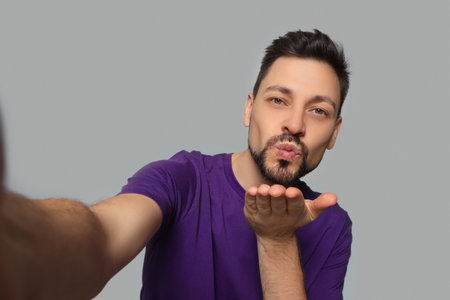Handsome man blowing kiss while taking selfie on light gray backgroundの写真素材