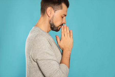 Man with clasped hands praying on turquoise backgroundの写真素材