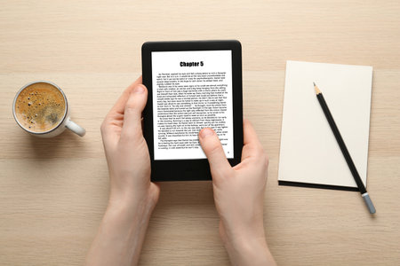 Woman using e-book reader at wooden table, top view