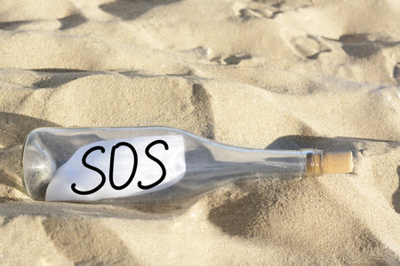 Glass bottle with SOS message on sand outdoorsの写真素材