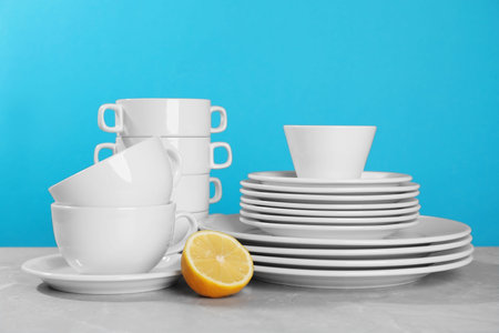 Clean tableware and half of lemon on gray table against light blue background