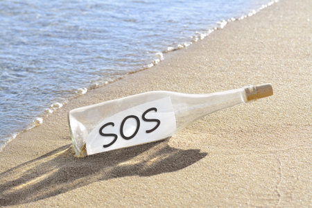 Glass bottle with SOS message on sand near seaの写真素材