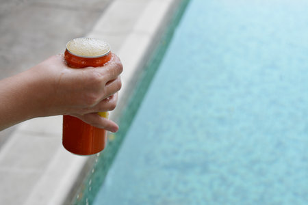 Woman holding tasty open canned beverage near swimming pool, closeup. Space for textの写真素材