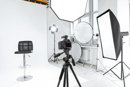Tripod with camera, bar stool and professional lighting equipment in modern photo studioの写真素材