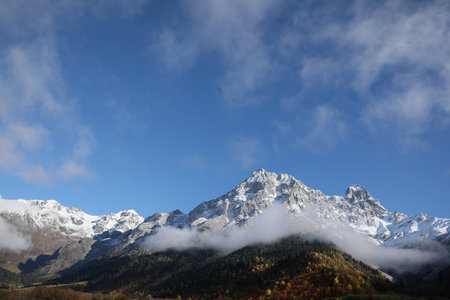Picturesque landscape of high mountains covered with thick mist under blue sky on autumn dayの写真素材