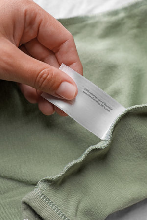 Woman holding clothing label on olive garment, closeup
