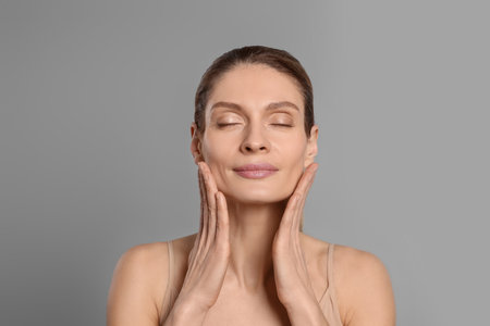 Woman massaging her face on gray backgroundの写真素材