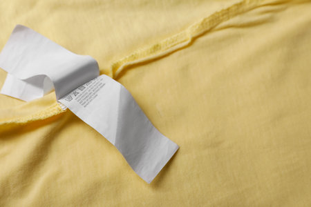 Clothing label on beautiful yellow garment, closeup. Space for textの写真素材