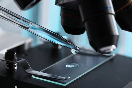 Dropping light blue liquid from pipette on glass slide in laboratory, closeupの写真素材