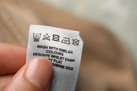 Woman holding clothing label of garment on blurred background, closeup. Space for textの写真素材