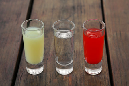 Shots with lime juice, tequila and sangria as colors of mexican flag on wooden table, closeup. traditional servingの写真素材