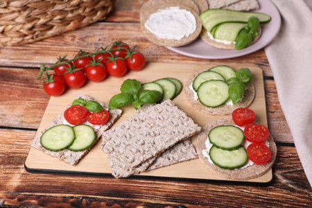 Tasty crispbreads, cucumber, tomatoes, cream cheese and basil on wooden tableの写真素材