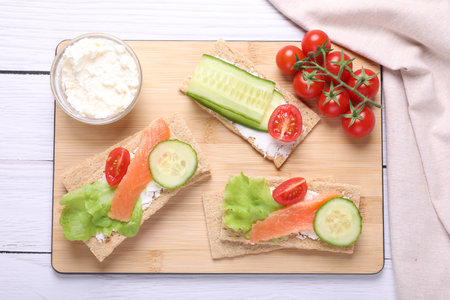 Tasty crispbreads with salmon, cream cheese, cucumber and tomato on white wooden table, top viewの写真素材
