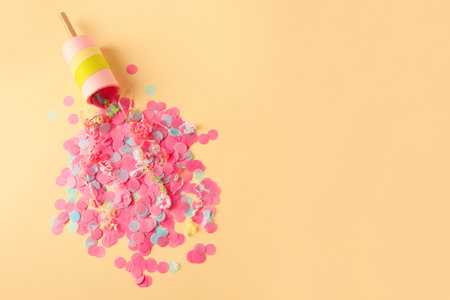 Colorful confetti and serpentine bursting out of party popper on beige background, flat lay. Space for textの写真素材