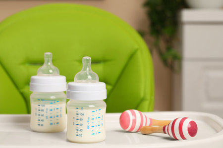 High chair with feeding bottles of infant formula and toy maracas on white tray indoorsの写真素材