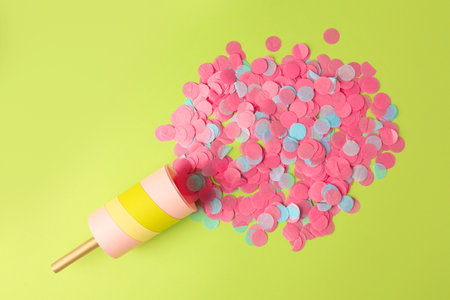 Colorful confetti bursting out of party popper on green background, flat layの写真素材