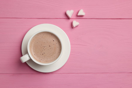 Cup of aromatic coffee and heart shaped marshmallows on pink wooden table, flat lay. Space for textの写真素材